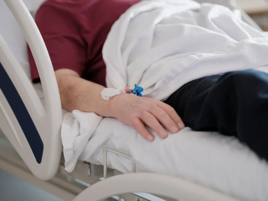 Patient resting in a hospital bed with an IV in the hand.