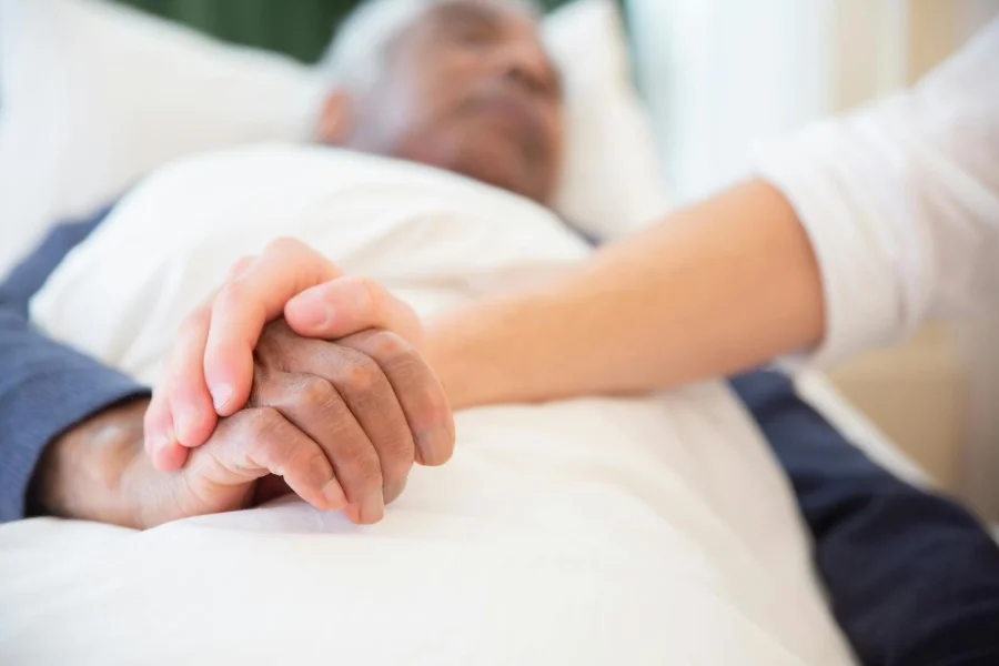 Patient and caregiver holding hands in a hospital bed.