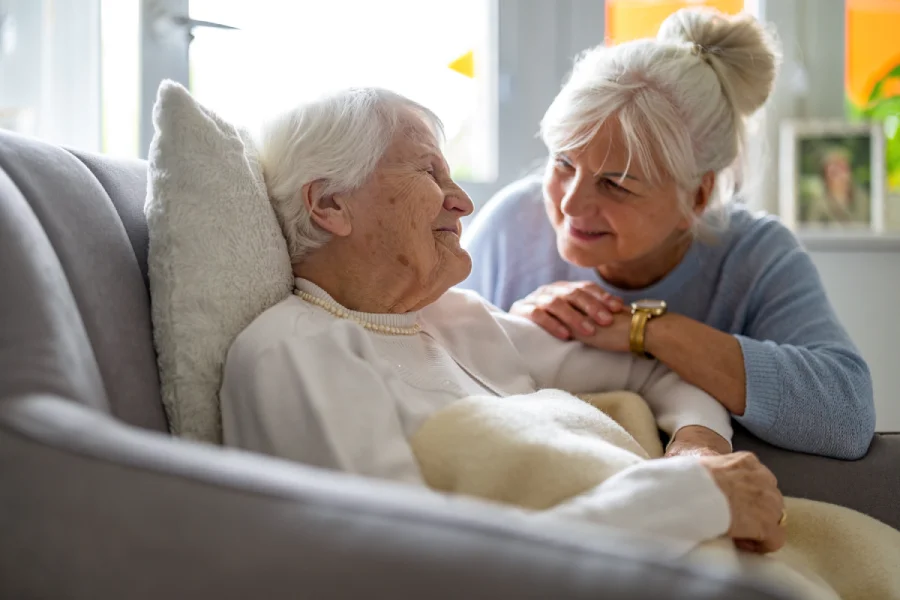 Senior woman smiling as a caregiver comforts her on a sofa.