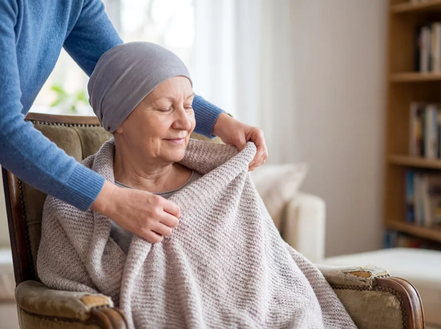 Caregiver gently wraps a blanket around an elderly woman sitting in a chair.