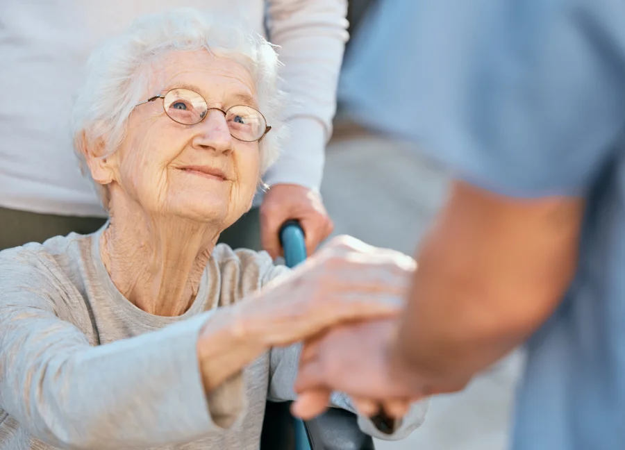 Elderly woman smiles while holding hands with a caregiver.